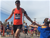 Male Runner with an orange shirt giving a child a high five at the 6 mile moment