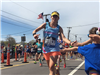 Female runner with a blue shirt and yellow visor gives kids high fives at the 6 mile moment