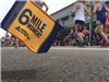 Image of 6 Mile Moment flag with runners and a building in the background from an angle at ground le