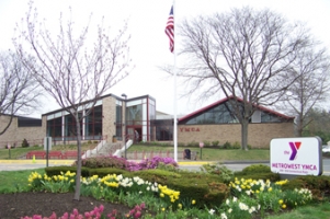 image of the front of the MetroWest YMCA - light brick building with a peaked roof and glass facade