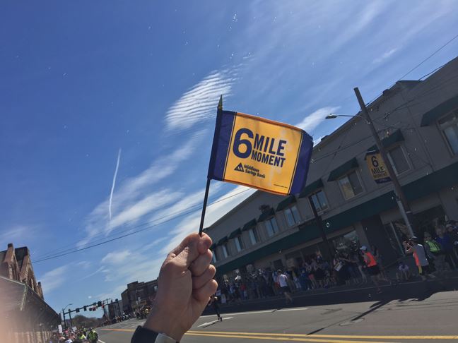Image of the 6 Mile Moment flag with the blue sky behind and a building in the background