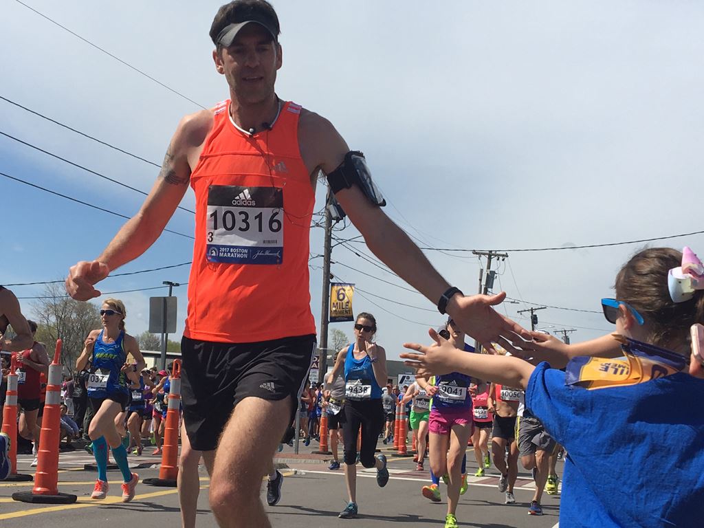 Male Runner with an orange shirt giving a child a high five at the 6 mile moment
