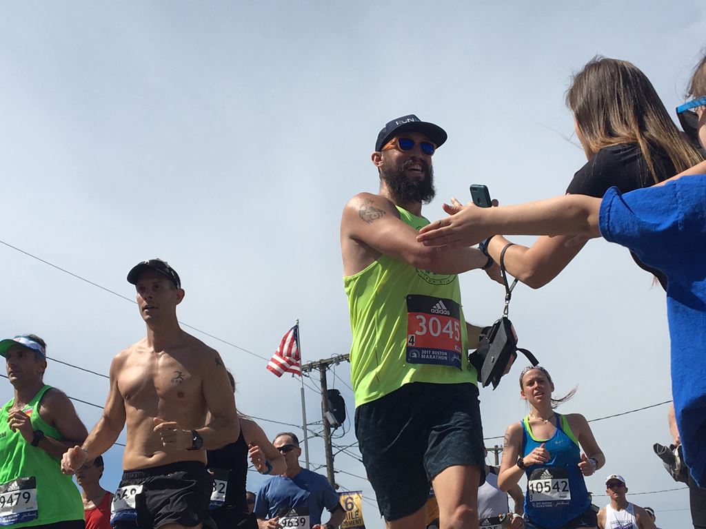 Runner with a beard and sunglasses smiles as he gives kids high fives with both hands