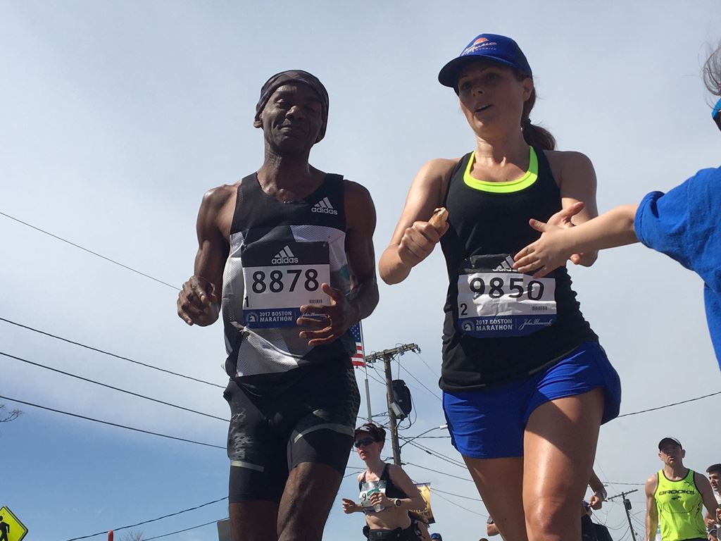 two runners one male and one female in black shirts give kids high fives as they pass