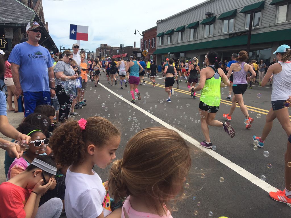 image of runners from the back and crowds facing them with bubbles floating around
