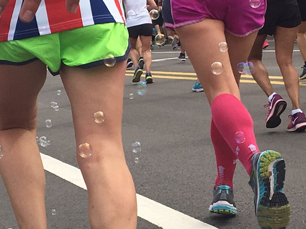 runner with British flag shirt and another with pink socks from the back with bubbles floating aroun