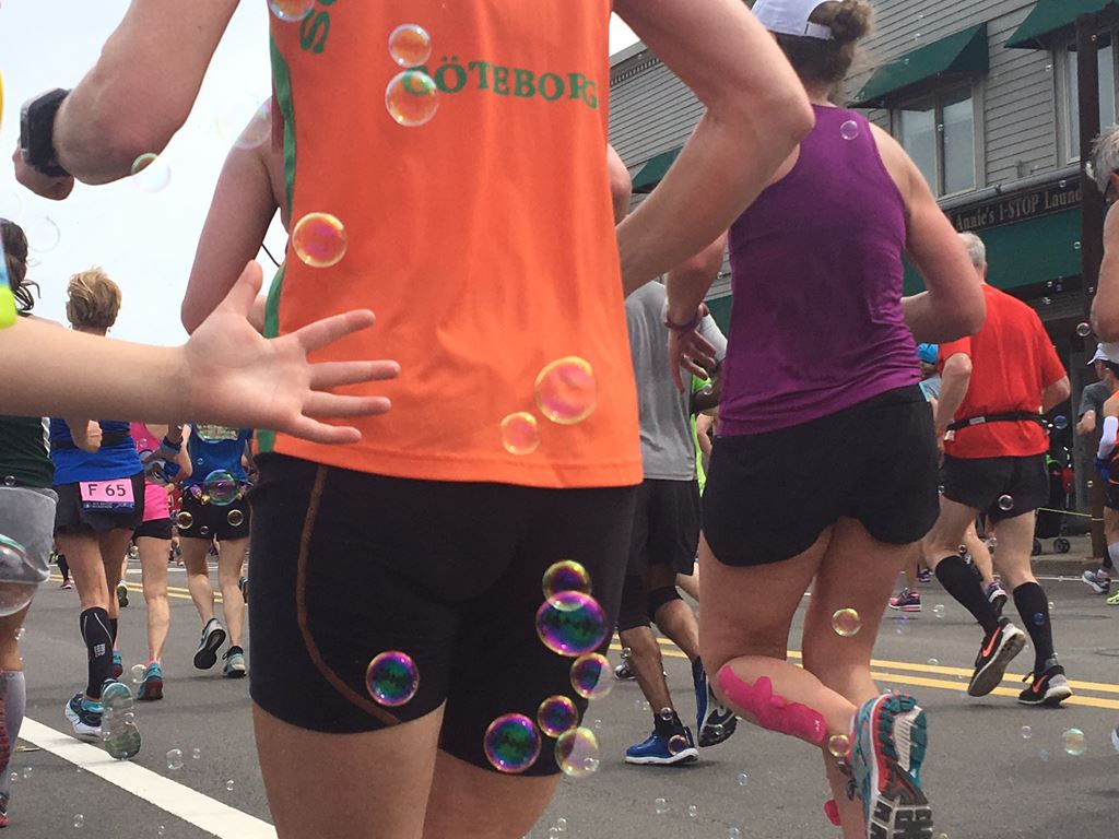 view of the back of a runner in an orange shirt with a child's hand and floating bubbles.